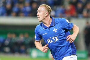 Fußballspieler von Darmstadt feiert nach Tor, Fans jubeln im Hintergrund. Intense Spielatmosphäre.