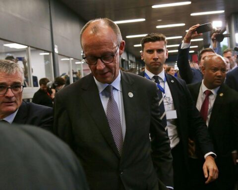 Friedrich Merz bei einer Pressekonferenz, umgeben von Journalisten und Mikrophonen.