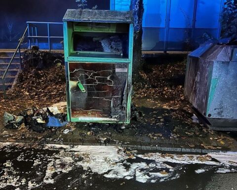 Beschädigter Altkleidercontainer nach Brand; Feuerwehr löschen, Polizei ermittelt wegen Brandstiftung.