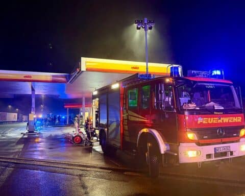 Brennender Pkw an Tankstelle, Feuerwehr im Einsatz, Nachtaufnahme, hohe Rauchentwicklung, dramatische Szene.