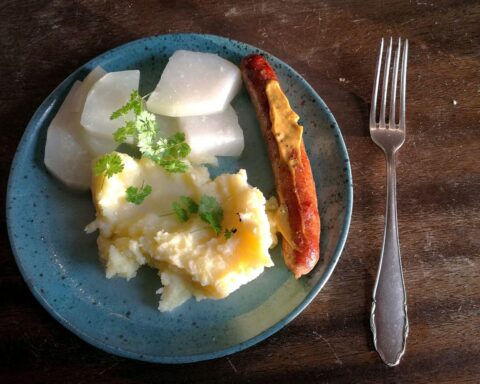 Bratwurst mit Kartoffelbrei und Kohlrabi auf einem Teller, symbolisiert regionale und preisbewusste Ernährung.