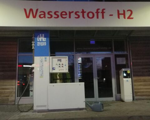 Wasserstoff-Tankstelle mit Menschen in Diskussion über Wasserstoff-Technologien und deren Zukunft.