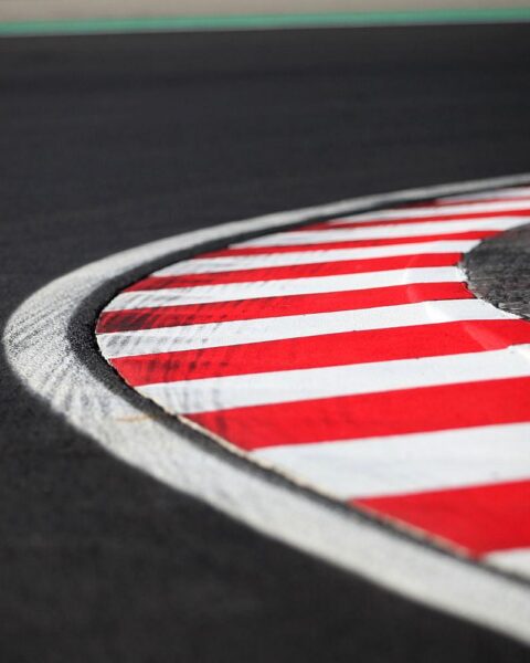 Formel-1-Rennstrecke mit markierten Fahrbahnlinien und enthusiastischen Motorsport-Fans im Hintergrund.