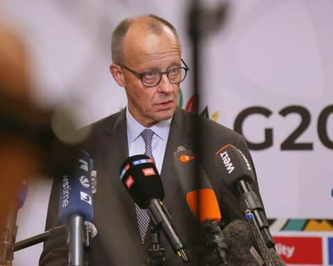 Friedrich Merz spricht, umgeben von kritischen Politikern und besorgten Bürgern. Spaltung sichtbar.