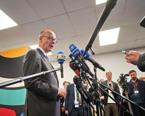 Friedrich Merz während einer Pressekonferenz, umgeben von Journalisten, mit ernster Miene.
