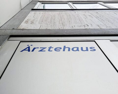 Ärztehaus im Hintergrund; Fokus auf sinkenden Krankenstand in großen deutschen Unternehmen.