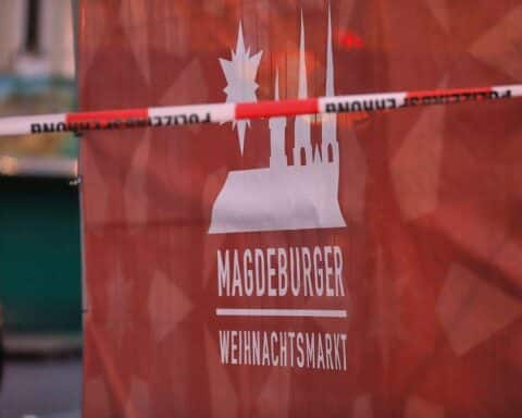 Weihnachtsmarkt-Atmosphäre mit festlicher Dekoration und Sicherheitsmaßnahmen im Vordergrund.