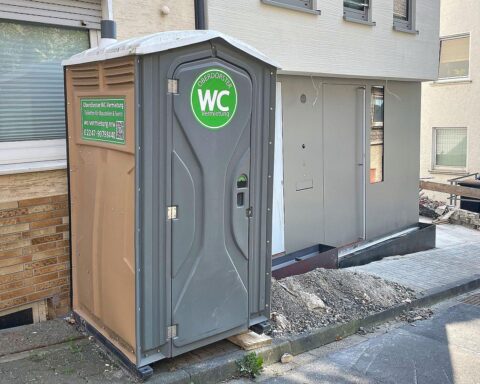 Mobile Toilettenkabine vor einem Neubau, symbolisiert den aktuellen Wohnungsbau in Nordrhein-Westfalen.