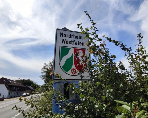 NRW-Landesschild vor Kölner Stadtlandschaft, symbolisiert neuen ESA-Standort und Forschungszentrum.