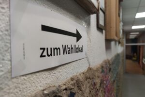 Wahllokal mit Wählern und Wahlurnen, Symbol für bevorstehende Stichwahl um Oberbürgermeisteramt.
