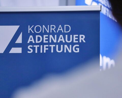 Konferenzraum mit Beamten und Politikern diskutiert Reformen der Bundesverwaltung. Dokumente und Laptops sichtbar.