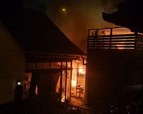 Ein brennendes Gartenhaus mit Feuerwehr und schwer verletztem Mann, dramatische Einsatzsituation.
