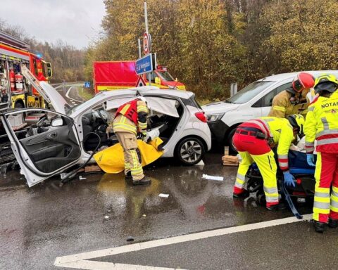 Drei kollidierte Autos, Feuerwehr im Einsatz, Verletzte werden behandelt, Unfallstelle abgesichert.