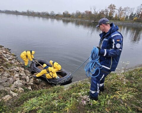 THW-Helfer im Schutzanzug bergen tote Vögel aus einem Schlauchboot am Gewässer.