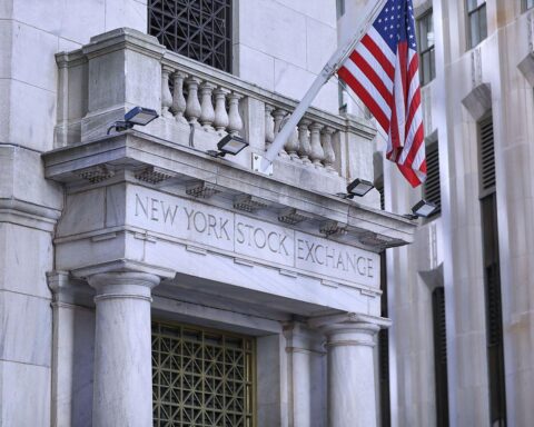 Aktienkurse steigen und fallen, Anleger erwarten wichtige Wirtschaftsdaten, NYSE im Hintergrund sichtbar.