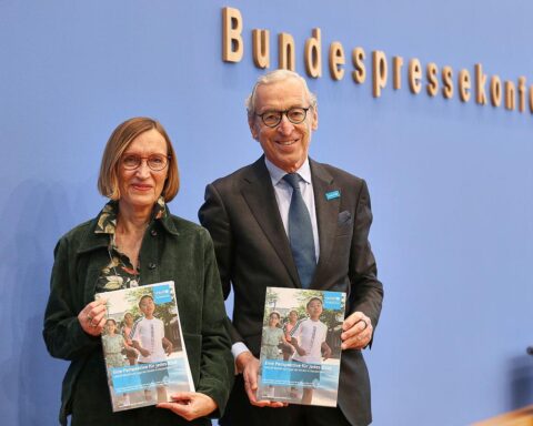 Ein besorgtes Kind, das mit leeren Händen in einem kargen Raum steht, symbolisiert Armut.