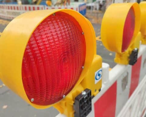Bild zeigt Straßensperrung mit Bauarbeiten, Sicherheitshinweisen und Feuerwehrfahrzeugen im Hintergrund.