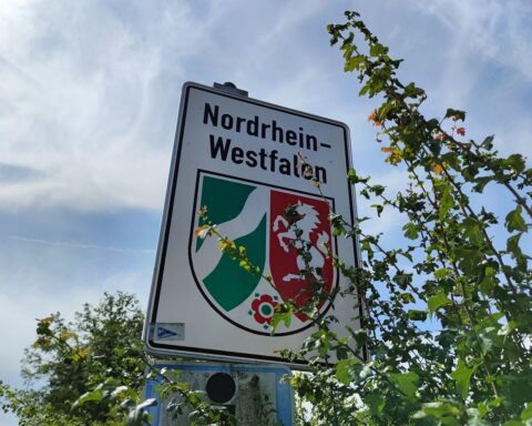 NRW-Landesschild vor Hintergrund von Auszubildenden, symbolisiert Bildung und Herausforderungen im dualen System.