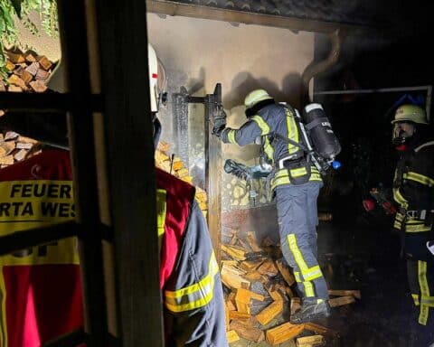 Feuerwehr löscht Brand in Costedt; brennende Mülltonnen und Brennholz am Carport.