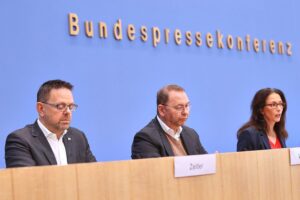 Zufriedene Mitarbeiter in einem Büro, Grafiken zu Arbeitszeiten und Krankheitsstatistiken im Hintergrund.