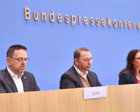 Zufriedene Mitarbeiter in einem Büro, Grafiken zu Arbeitszeiten und Krankheitsstatistiken im Hintergrund.