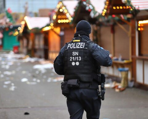 Weihnachtsmarkt mit Sicherheitskräften, Glühweinstand, festlicher Beleuchtung und Menschen, die friedlich feiern.