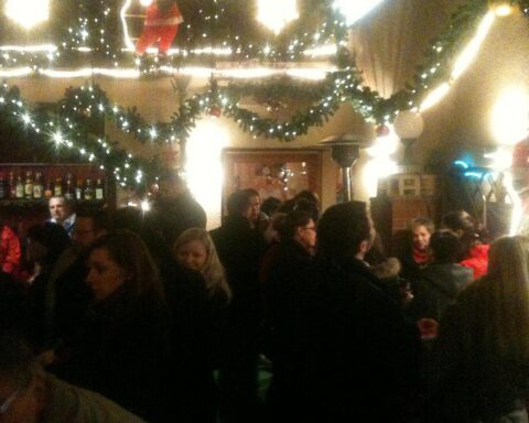 Weihnachtsmarkt mit festlicher Stimmung, singenden Menschen und festlich dekorierten Ständen vor dem Dom.