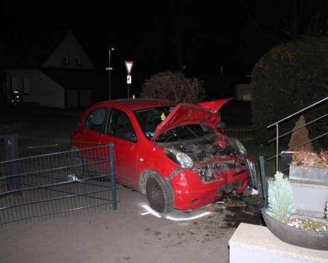 Ein beschädigter Nissan Micra im Vorgarten, umgeben von Polizei und Zaunresten.