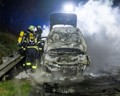 PKW-Brand auf Autobahn mit Feuerwehr im Einsatz, rauchende Trümmer und gesicherte Unfallstelle.