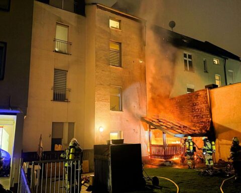 Feuerwehr im Einsatz, Brand an Terrasse eines Mehrfamilienhauses, verrauchte Fassade, Feuerwehrkräfte arbeiten.