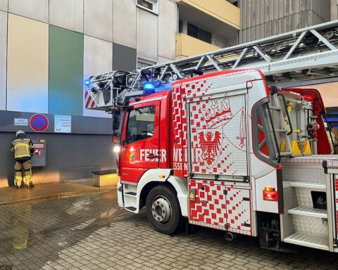 Drehleiter der Feuerwehr bereitstehend vor Hochhaus, Einsatzkräfte bekämpfen Brand im 12. Obergeschoss.