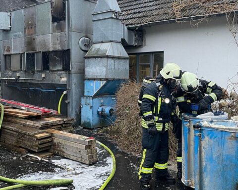 Feuerwehr im Einsatz bei Brand in Schreinerei; Rauch und Löschmaßnahmen sichtbar.