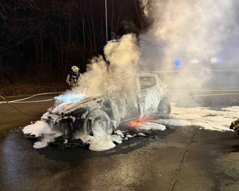 Brennendes Auto auf Rastplatz, Feuerwehr im Einsatz, Rauch und Löscharbeiten sichtbar.