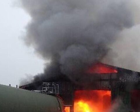 Brandende Lagerhalle mit starkem Rauch, Feuerwehr im Einsatz, große Schäden sichtbar.