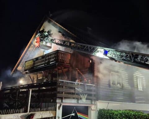 Einsatz der Feuerwehr bei Wohnhausbrand mit Drehleiter und Rettungsmaßnahmen für Verletzte.