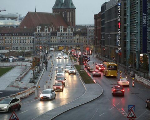 Auto mit Verbrennungsmotor auf der Straße, umgeben von Verkehrszeichen und urbaner Umgebung.