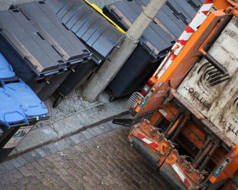 Mülltonnen und Müllabfuhrwagen symbolisieren steigende Abfallgebühren in Köln. Gebührenschilder im Fokus.