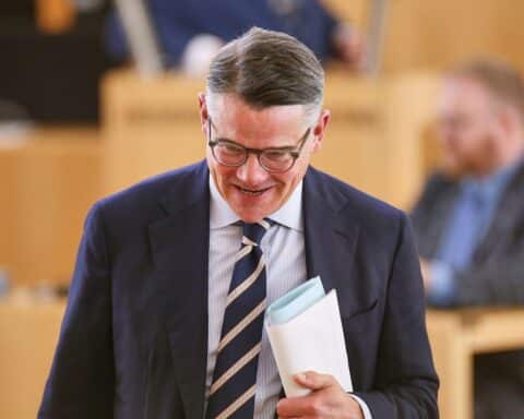 Boris Rhein diskutiert Personalpolitik und Verbeamtungsstopp in Hessen, Zeitung im Hintergrund, nachdenklicher Ausdruck.