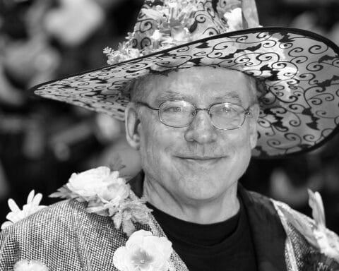 Ein Porträt von Rosa von Praunheim, umgeben von Filmpostern und Symbolen der LGBTQ+-Bewegung.