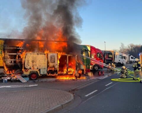 Feuerwehr im Einsatz gegen großen Fahrzeugbrand auf Autobahn mit Rauch und Flammen.