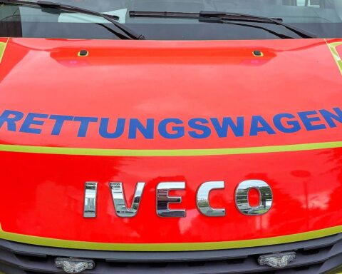 Verkehrsunfall: Rettungsengel, verletzt, Einsatzkräfte vor Rettungswagen, zerstörte Fahrzeuge, gesperrte Straße.
