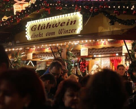 Besucher genießen Glühwein an einem Weihnachtsmarktstand, trotz Unsicherheiten und steigenden Kosten.