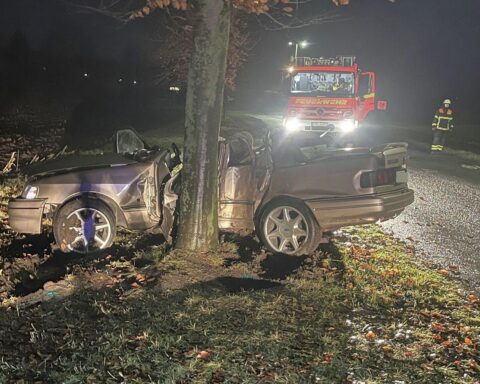 Ford Sierra prallt gegen Baum, Rettungskräfte sichern Unfallstelle, zwei Männer schwer verletzt.