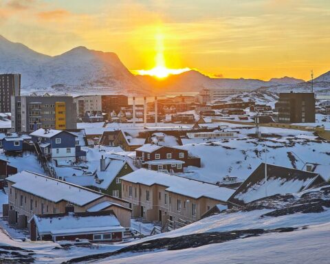 Landschaft von Nuuk, Grönland: schneebedeckte Berge, buntes Stadtbild, polarer Himmel und maritime Elemente.