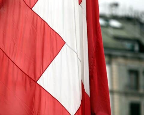 Schweizer Flagge mit traurigem Hintergrund einer Silvesterexplosion in Crans-Montana.