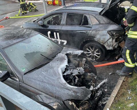 Zwei brennende Autos vor einem Mehrfamilienhaus, Feuerwehr unter Kontrolle und Absperrung.