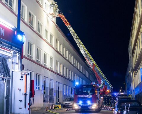 Einsatzkräfte der Feuerwehr bei Verpuffung in Mehrfamilienhaus, beschädigte Decke und Einsatzfahrzeuge sichtbar.