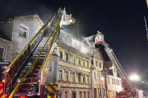 Drehleiter im Einsatz, Feuerwehrkämpfer am Gebäude; starke Rauchentwicklung, Einsatzkräfte retten Personen.