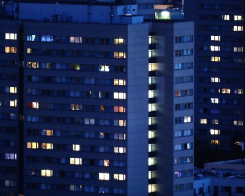 Dunkle Wohnungen mit beleuchteten Fenstern, Symbol für steigende Energiekosten und Preisanalyse.