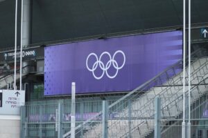 Kampagne für Olympia-Bewerbung Köln-Rhein-Ruhr startet Olympische Ringe vor urbanem Hintergrund, symbolisieren Bewegungseinschränkungen und Sicherheitsbedenken in Hamburg.
